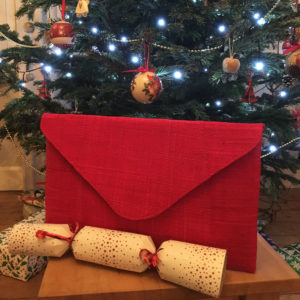 Red envelope clutch bag with Christmas cracker in front of Christmas tree