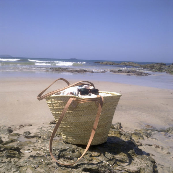 Double handle beach basket at the seaside filled with sarongs and towels