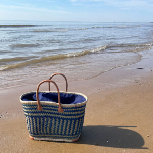 Large blue drawstring shopper basket on the beach beside the sea