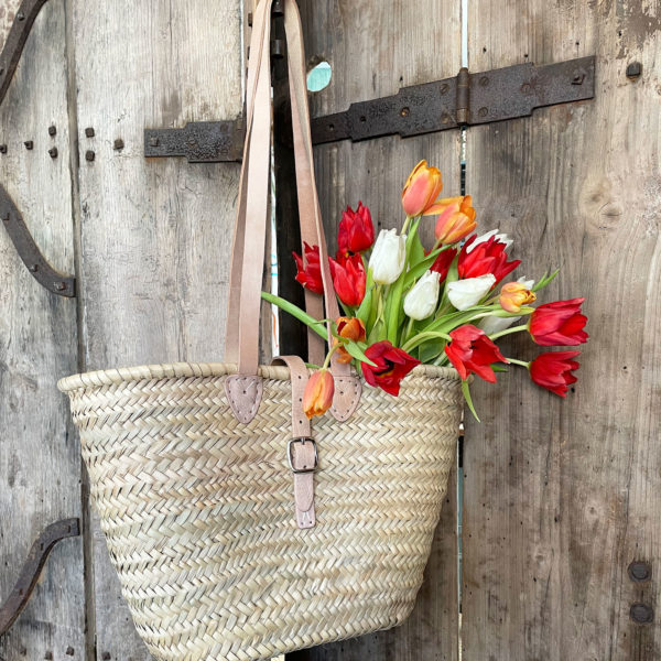 Long handle basket with a buckle fastening filled with tulips hanging on a door