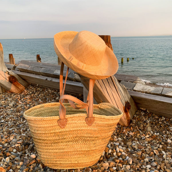Small double handle basket with natural mimosa sun hat at the beach