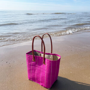 Small pink pinstripe basket bag on a beach beside the sea