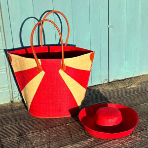 Red sunburst raffia tote bag with red raffia mimosa sun hat beside a beach hut