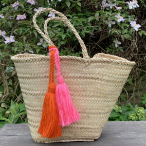 Hot pink and orange wool tassels tied to a palm handle basket