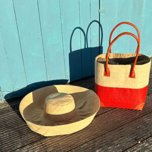 Large Mimosa Hat in natural with Hanta Two Tone natural and coral tote bag beside a beach hut