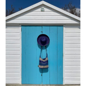 Blue crossbody bag with a raffia hat hanging on a beach hut door