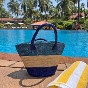 Crochet bucket bag in blue stripes beside a pool in Goa