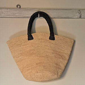 Crochet bucket bag in natural with black handles hanging on a hook
