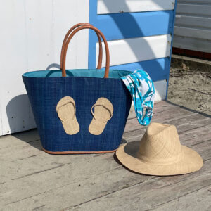 Turquoise flipflop bag by a beach hut with a Panama hat
