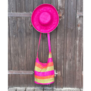 Brightly coloured crossbody bag with a raffia hat hanging on a beach hut door