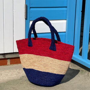 Red natural and blue stripe crochet bag beside a beach hut