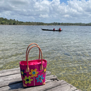 Raffia tote bag in pink with flowers stems beside a lake in Madagascar