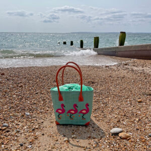 Small raffia tote bag with flamingos embroidered on one side at the beach