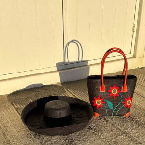 Small red sunflower tote bag with large black raffia mimosa hat at beach