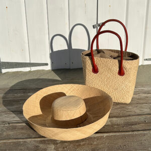 Camille raffia tote bag in natural with a large Mimosa raffia hat in natural beside a beach hut
