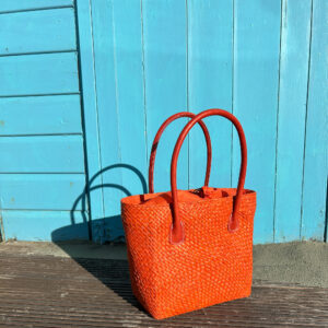 Camille raffia tote bag in orange beside blue beach hut