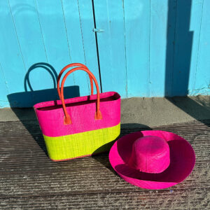 Monique raffia handbag with zip fastening in lime and pink with pink Mimosa raffia hat beside a blue beach hut