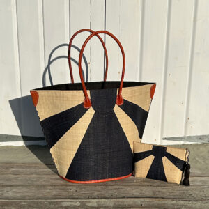 Sunburst beach bag and clutch bag in black beside a beach hut